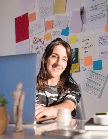 Young woman typing on her laptop and smiling at the camera in a workspace